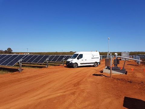 A white van is parked in a field of solar panels.