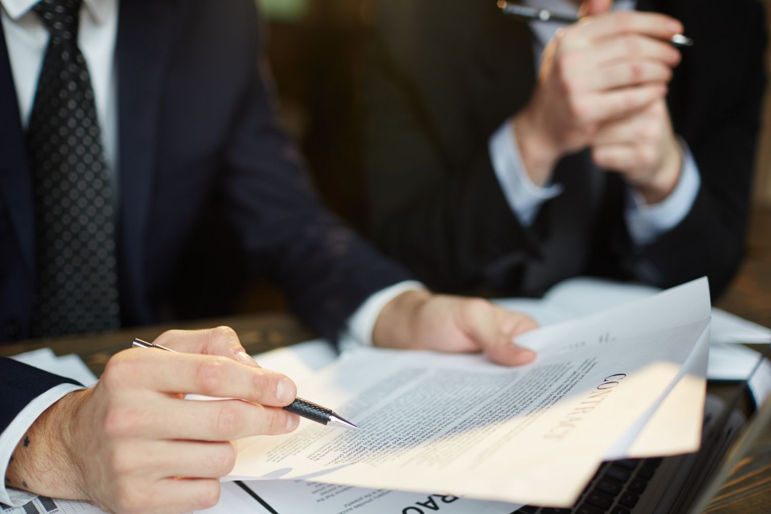 Two people in suits reviewing documents, one pointing with a pen.
