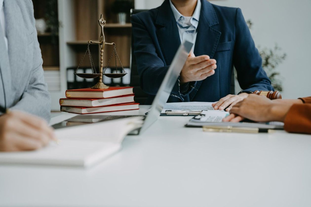 Lawyers in suits at a table with scales of justice and legal books, discussing paperwork.