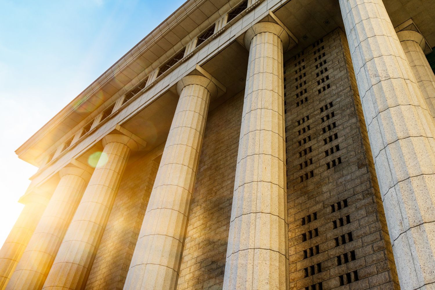 Stone building with large columns, sunlight shining from the left.