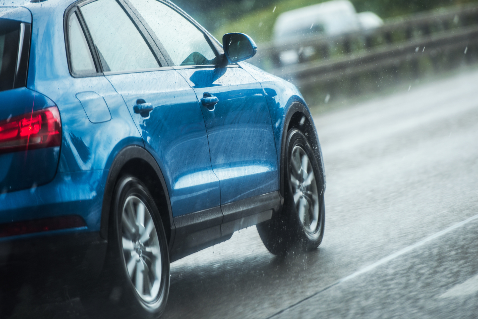 Blue car driving on wet road in the rain.