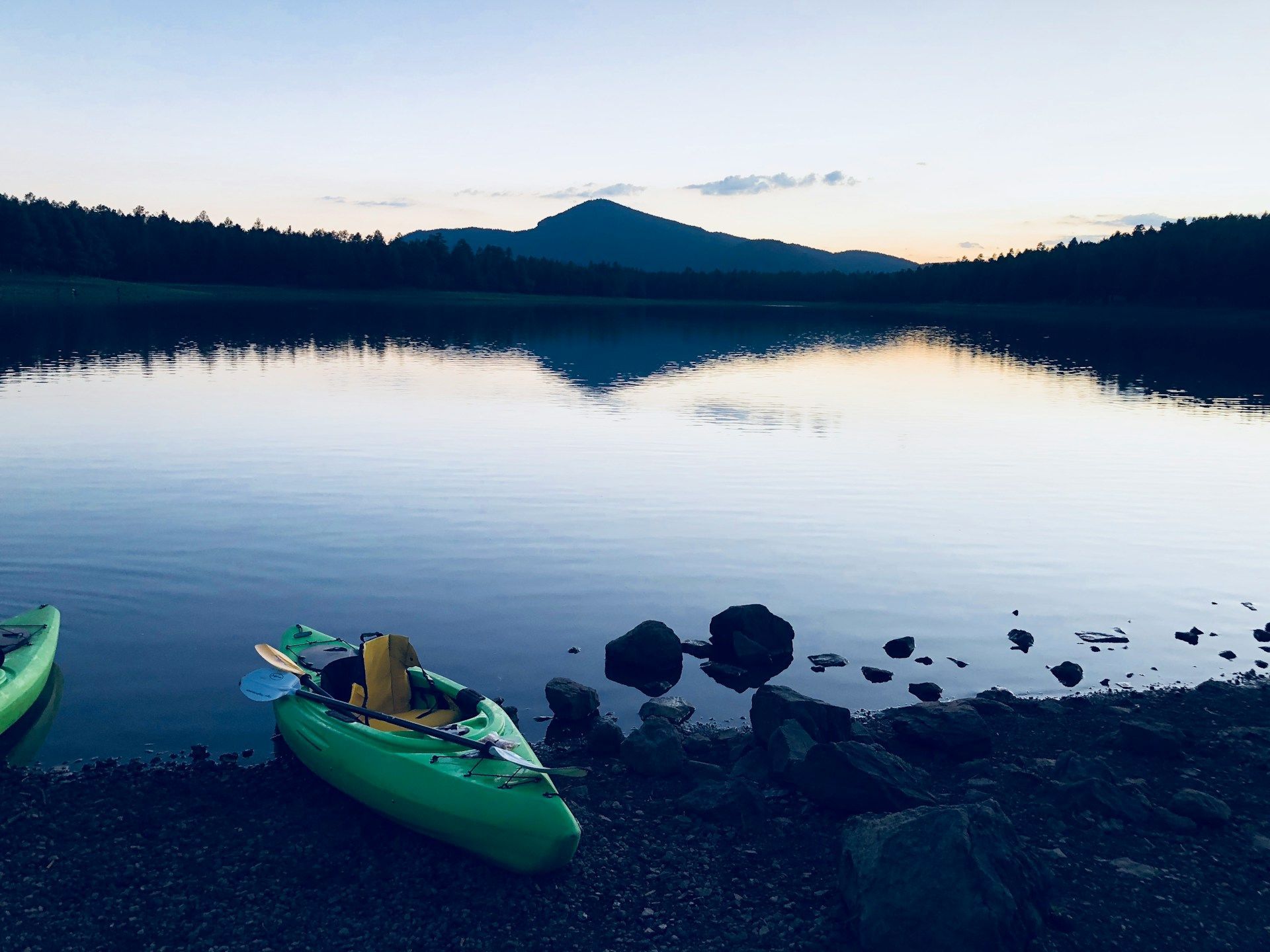 Green kayak by a lake at dusk, mountain reflection in water.
