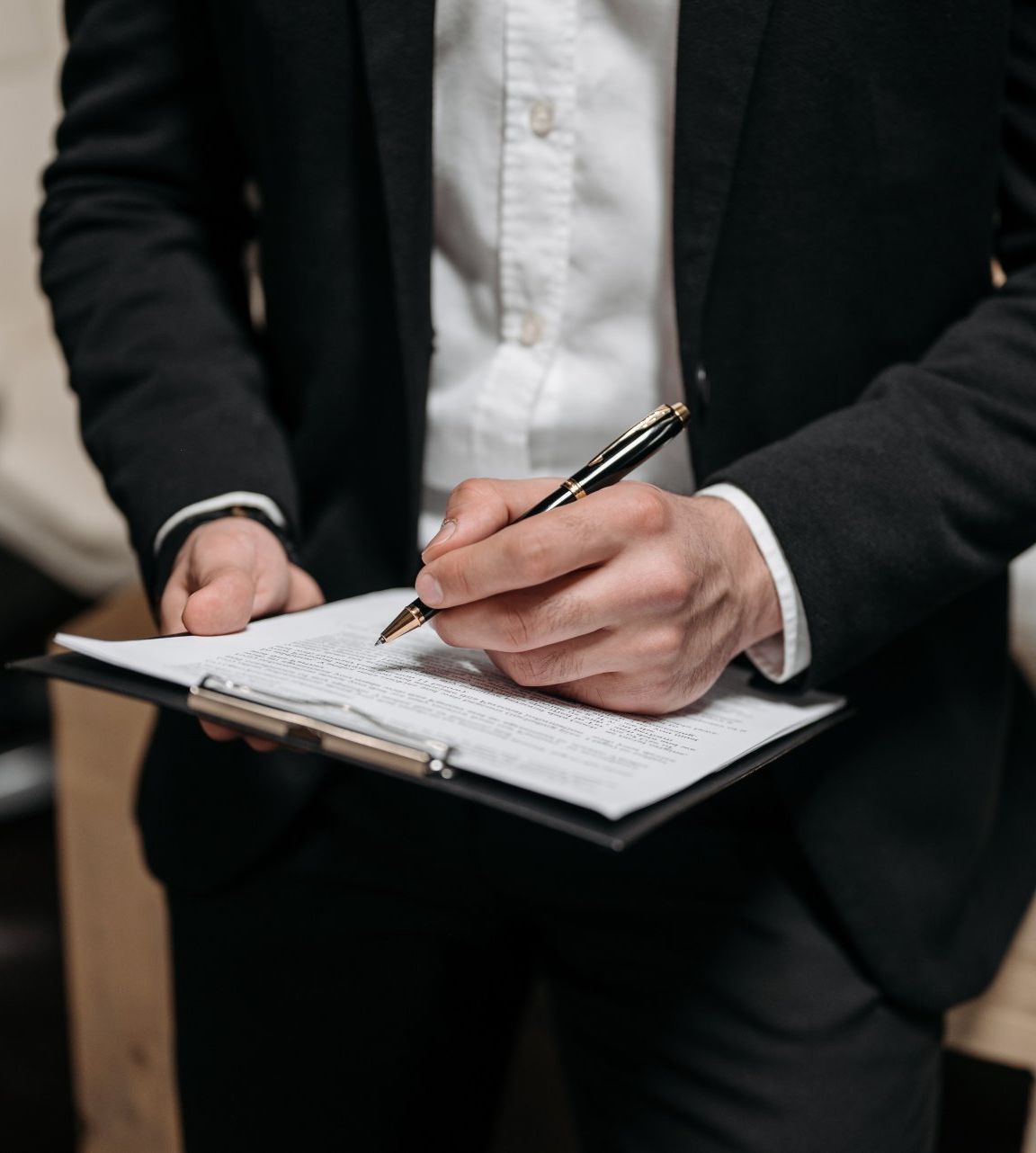 Person in a suit writing on a clipboard, holding a pen.