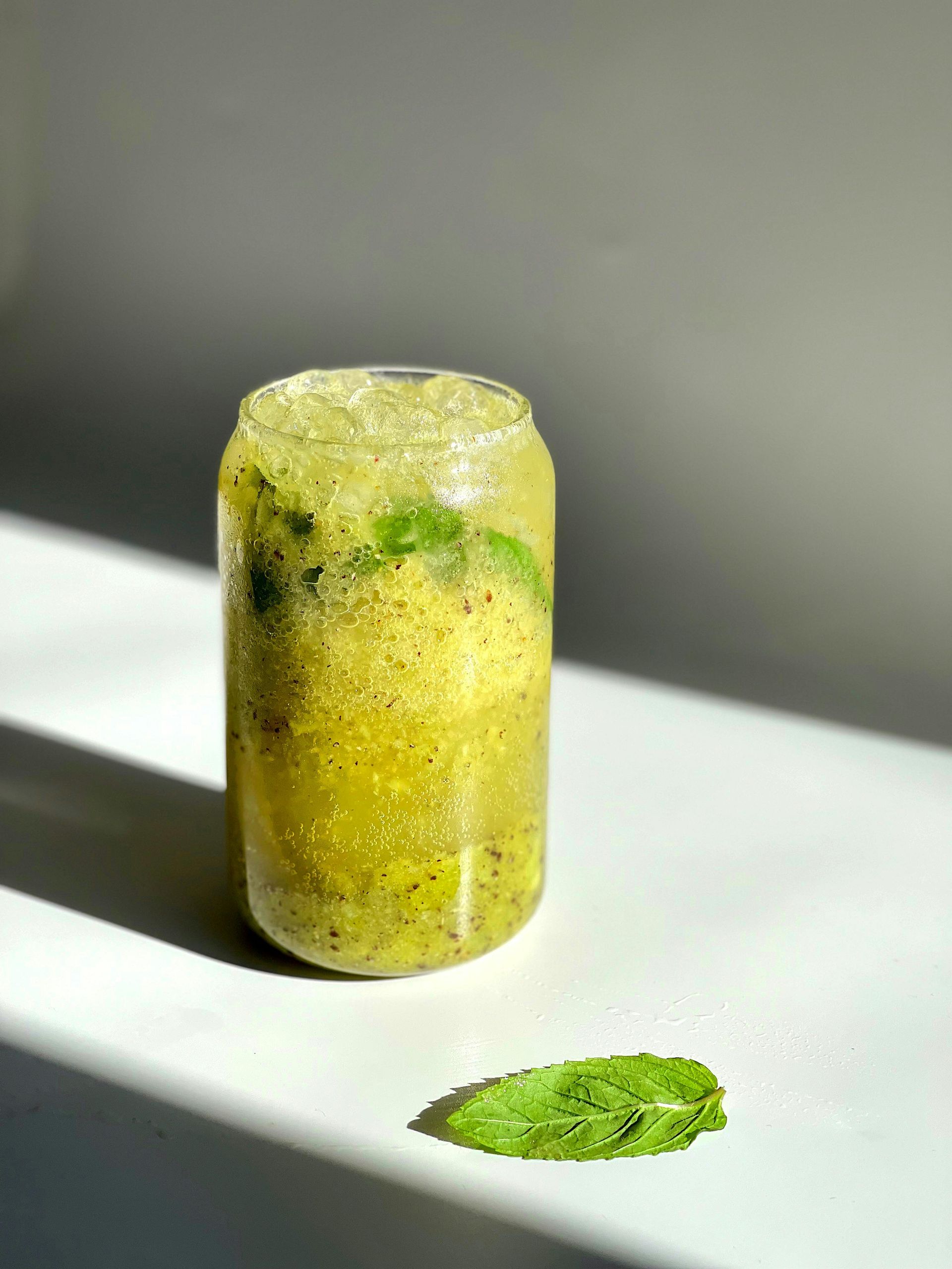 Un verre de limonade est posé sur une table à côté d'une feuille de menthe.