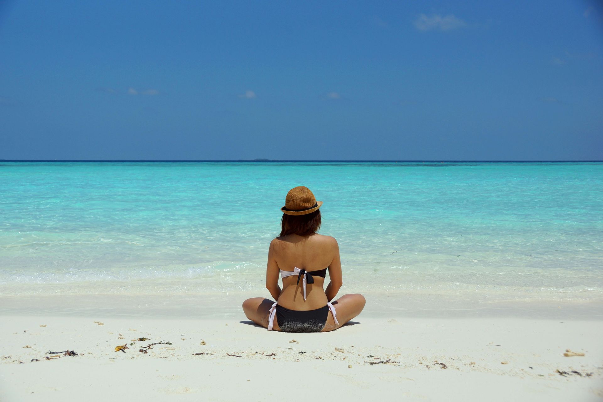 Une femme en bikini est assise sur la plage et regarde l'océan.