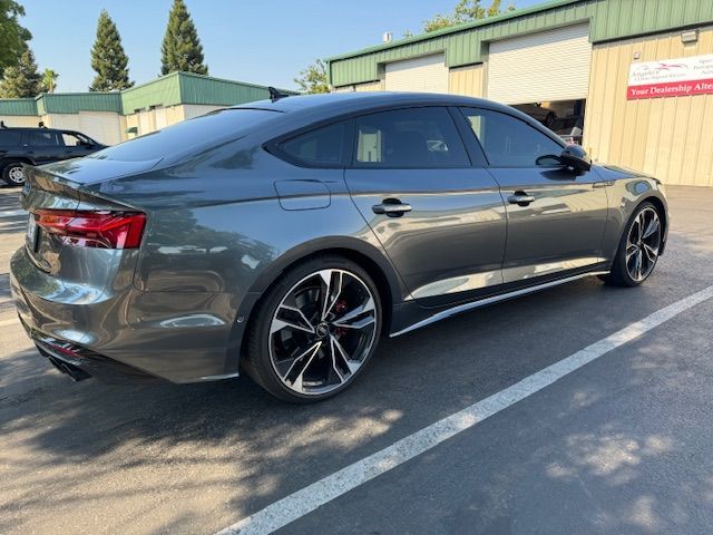 Gray sedan parked in a lot beside industrial buildings, side view