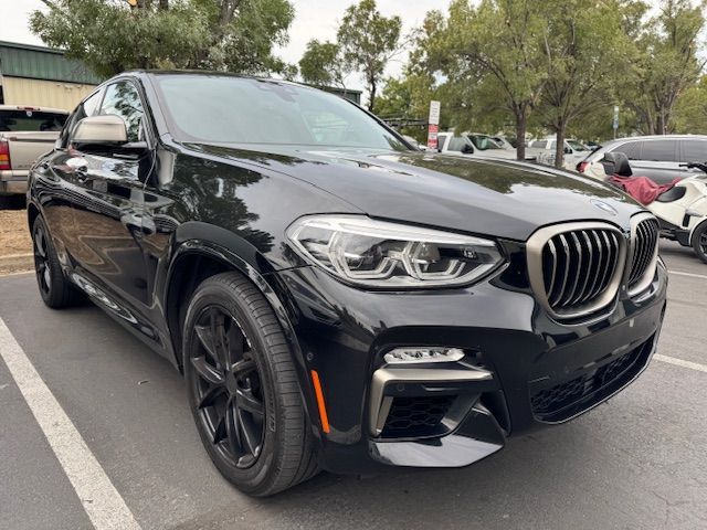 Black BMW SUV parked outdoors in a lot, front-left view with trees and other cars in the background
