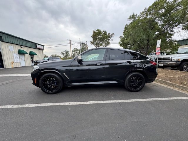 Black sedan parked in a lot beside a building under cloudy skies