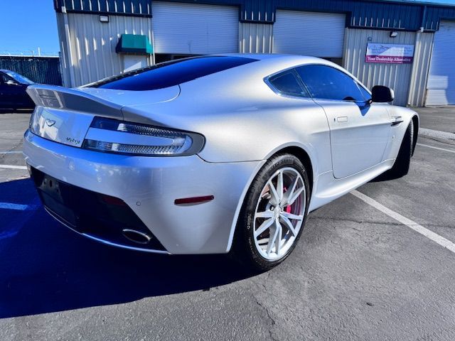 Silver sports coupe parked outside a blue industrial building, rear three-quarter view