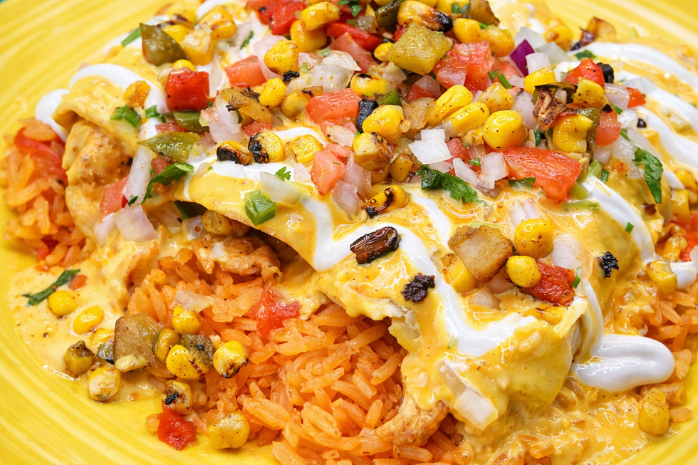Mexican-style enchiladas topped with white sauce, salsa, corn, and beans on a yellow plate