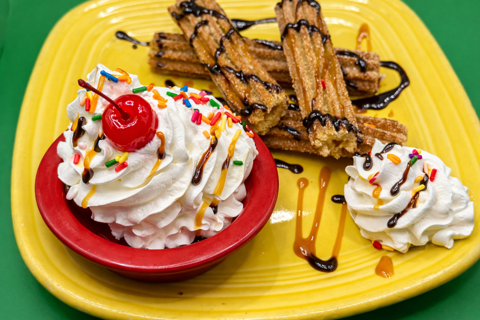 Dessert plate with whipped cream, cherry, waffle rolls, chocolate drizzle, and a scoop on a yellow plate