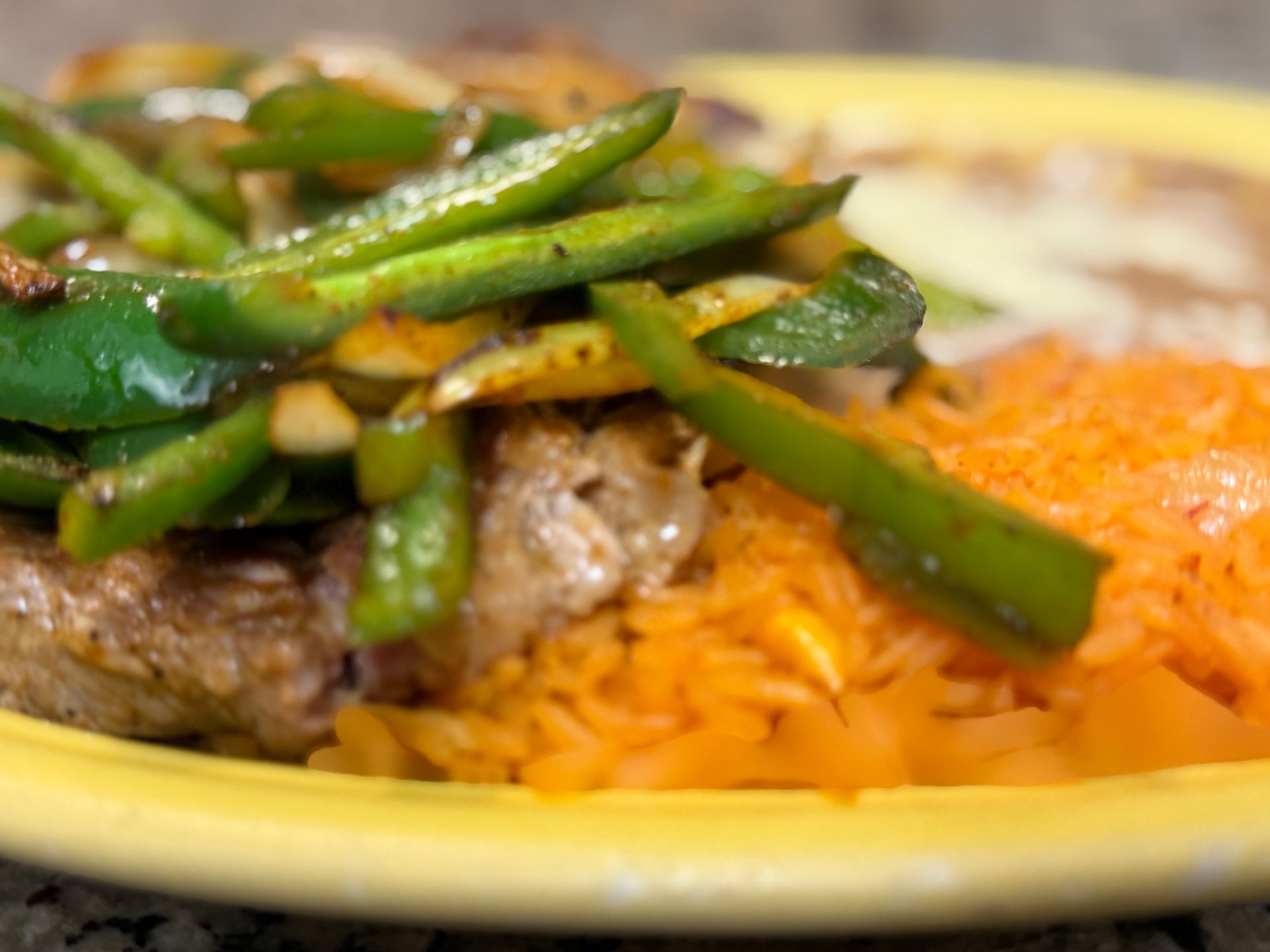 Stir-fried green peppers and meat over rice and orange shredded topping on a yellow plate