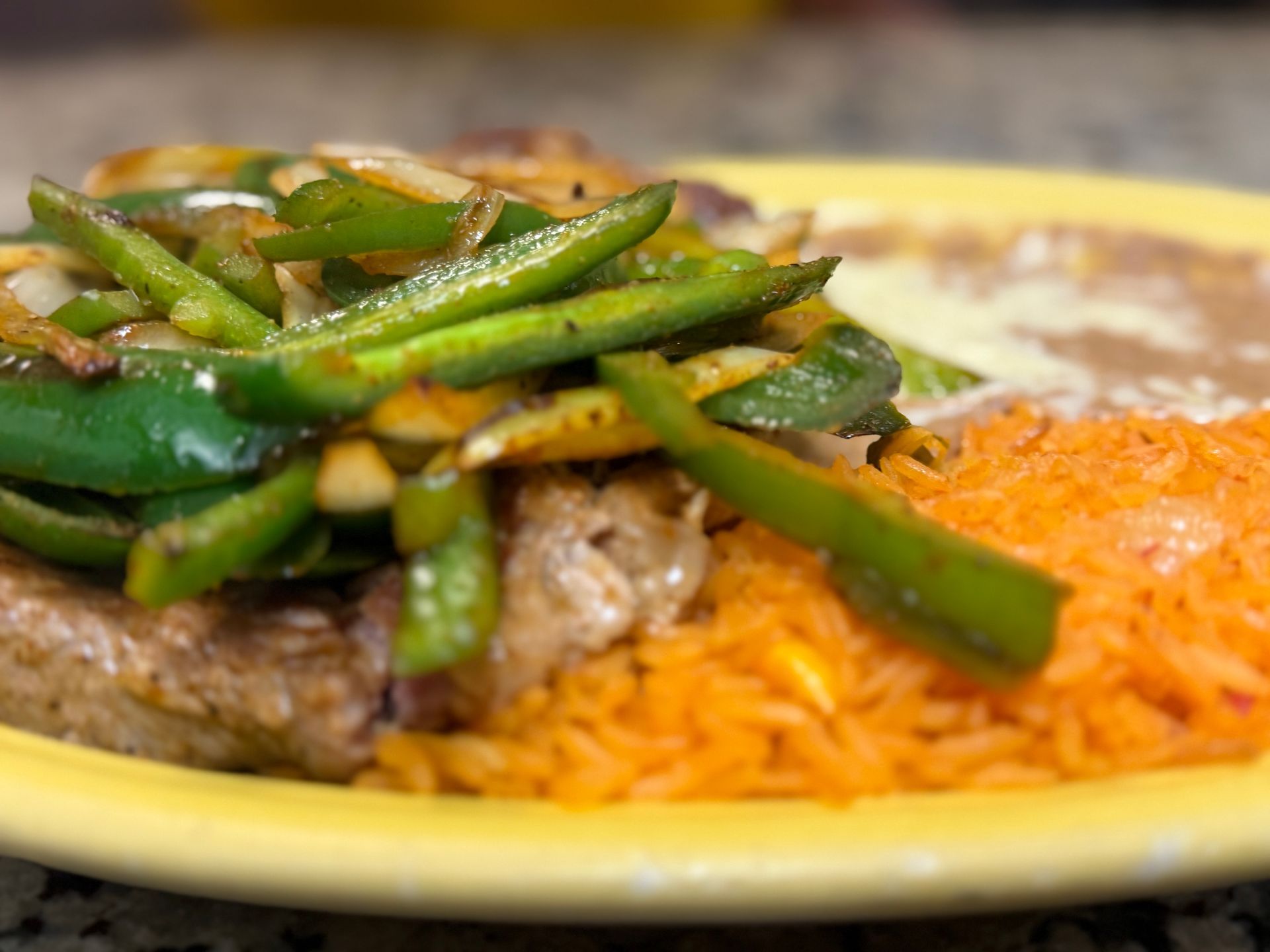 Plate of rice with grilled meat and green peppers on a yellow dish