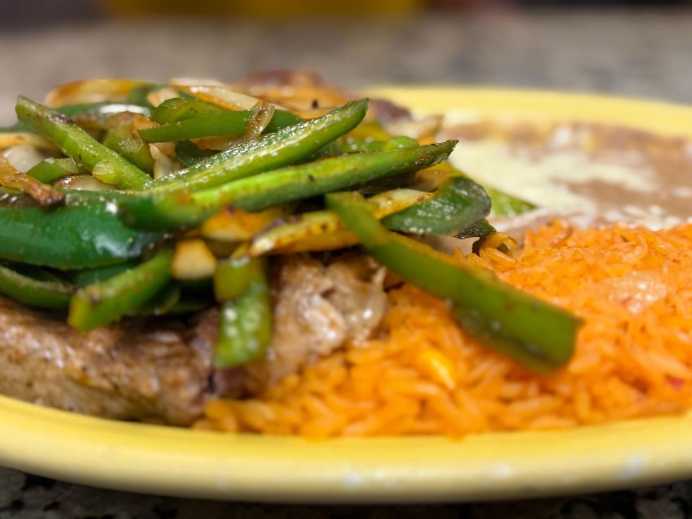 Plate of rice with grilled meat and green peppers on a yellow dish