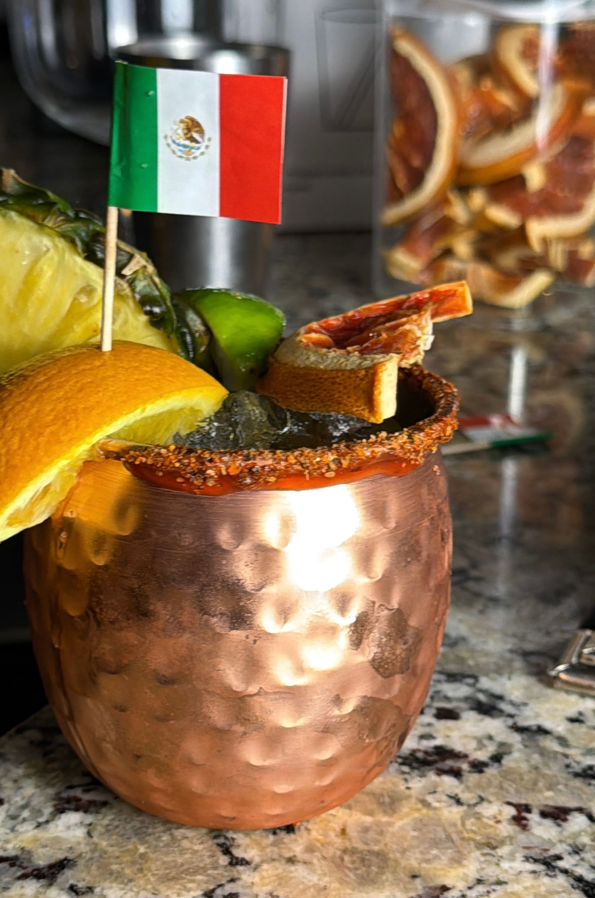 Copper mug with a Mexican flag, lime, and fruit garnish on a bar counter