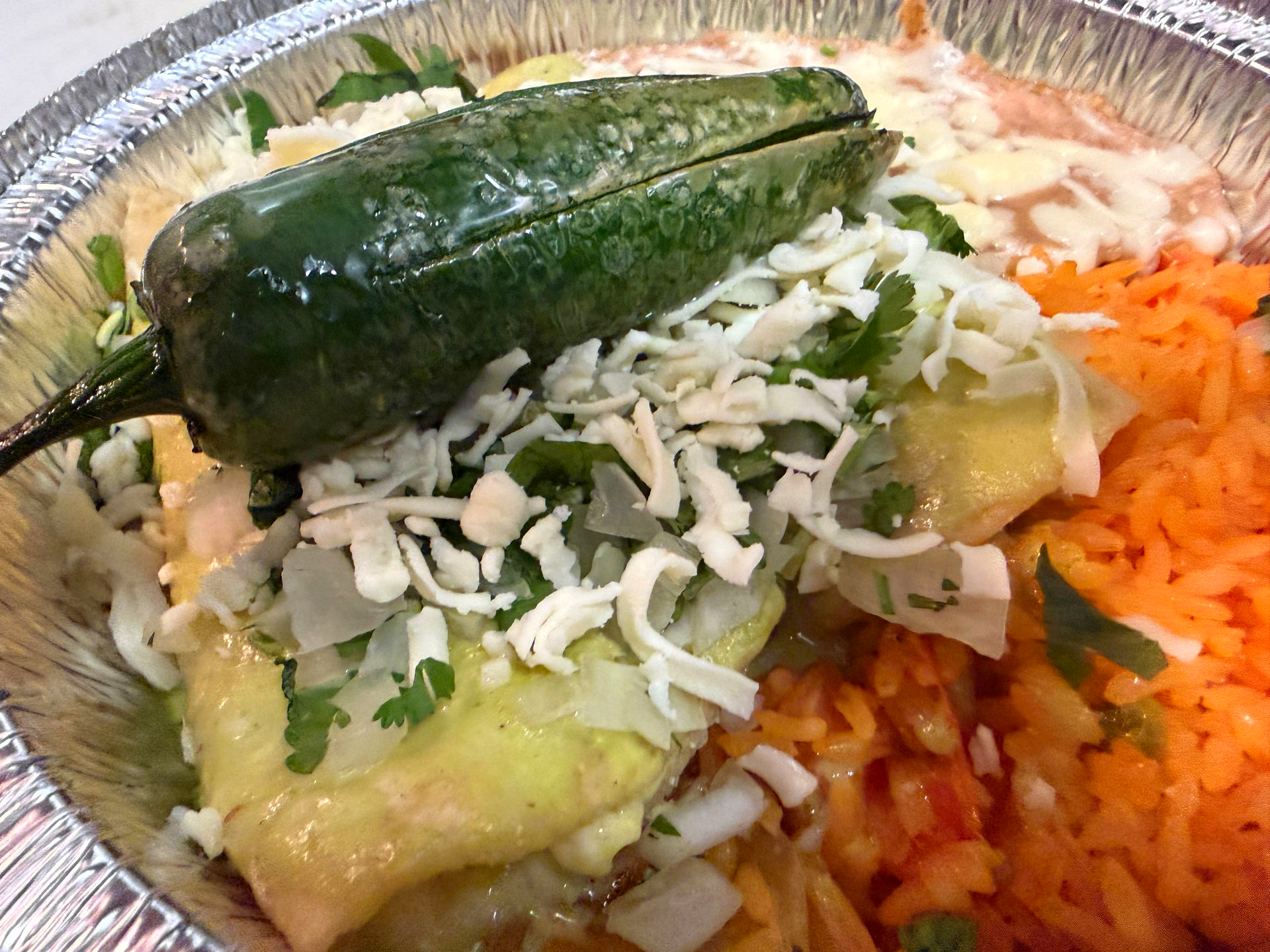Taco with roasted pepper, shredded cheese, cilantro, and orange rice in a foil tray