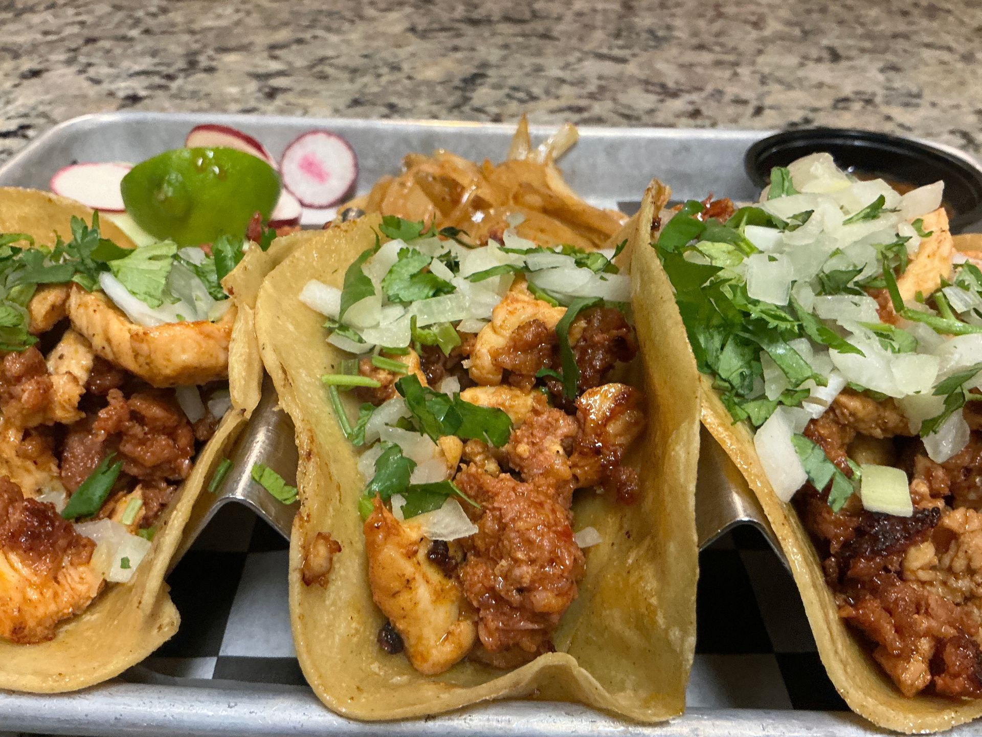 Tacos al pastor topped with cilantro, onions, and lime on a tray with salsa.