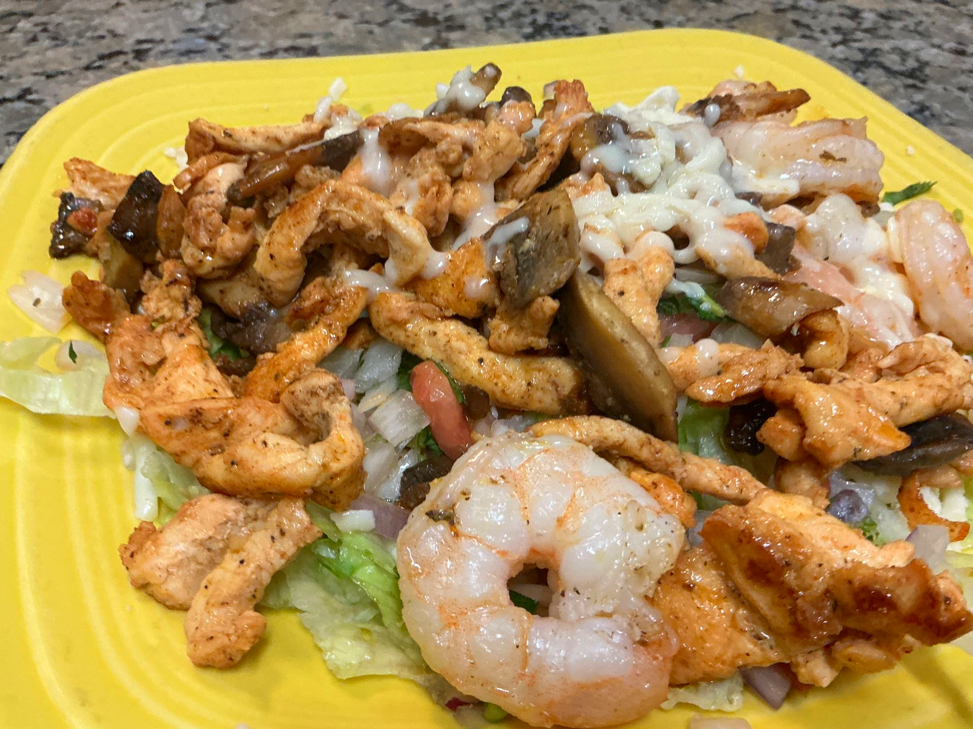 Yellow plate of grilled chicken and shrimp over lettuce, topped with creamy sauce.