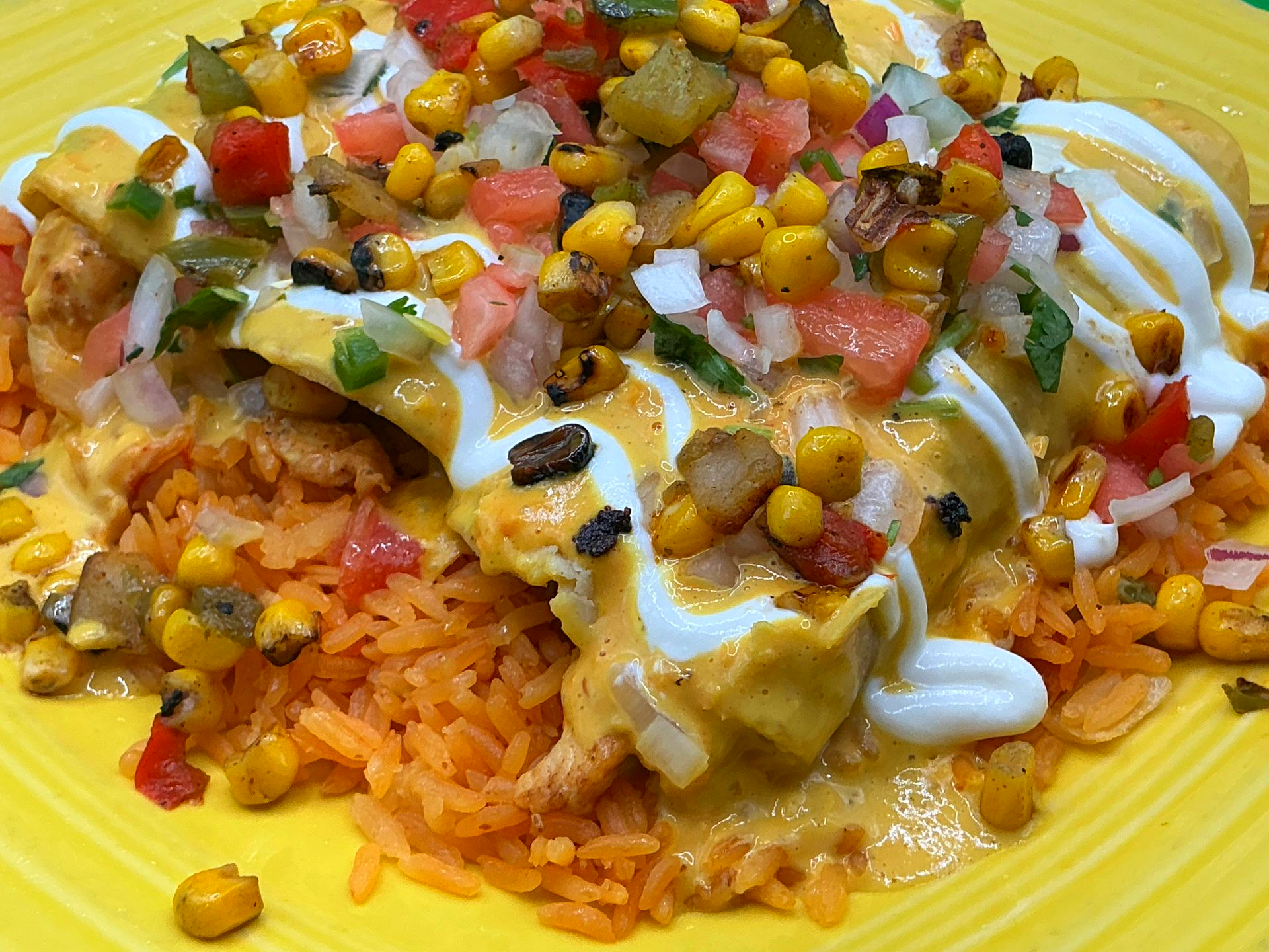 Rice topped with cheese, corn, diced tomatoes, cilantro, and sour cream on a plate