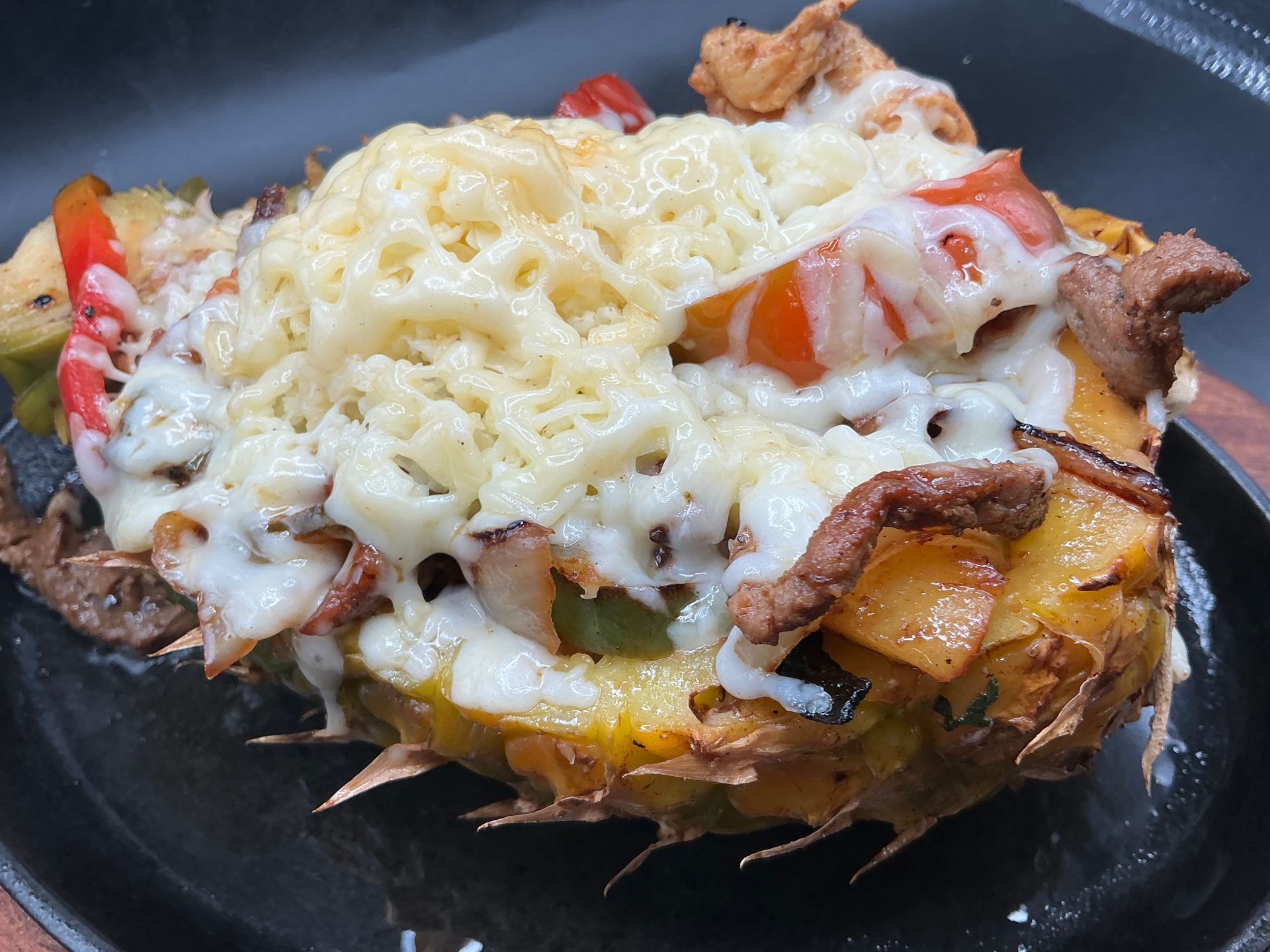 Baked stuffed potato topped with melted cheese, tomato, and browned meat on a black plate