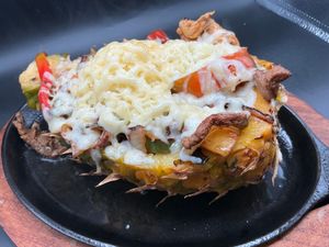 Grilled stuffed pineapple boat with melted cheese, peppers, and meat on a black plate