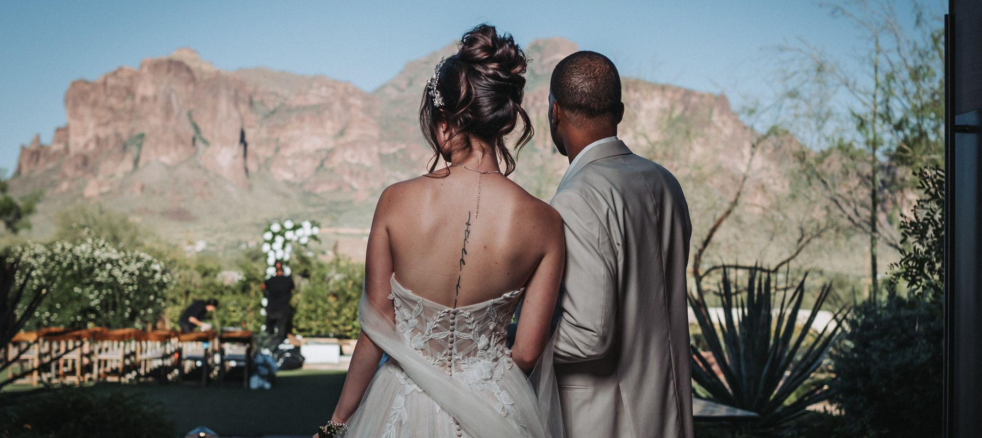 Bride and groom looking toward wedding ceremony with mountain backdrop.