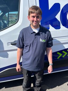Person standing beside a white vehicle with blue graphics, wearing a navy polo and black pants.