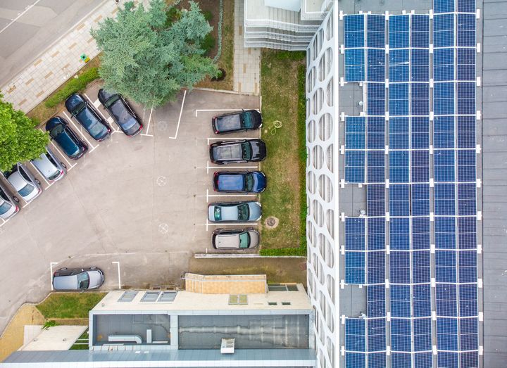 Aerial view of a parking lot beside a building with blue solar panels on the roof.