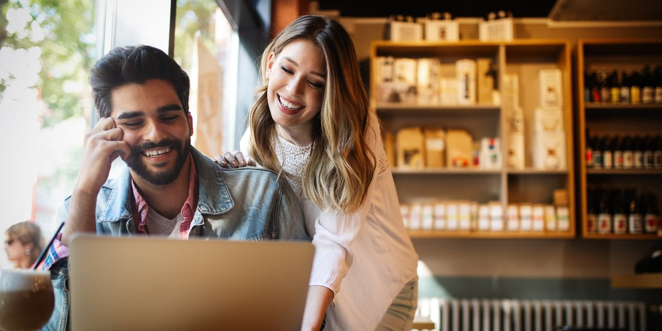 Two coworkers smiling over a laptop in a cozy café