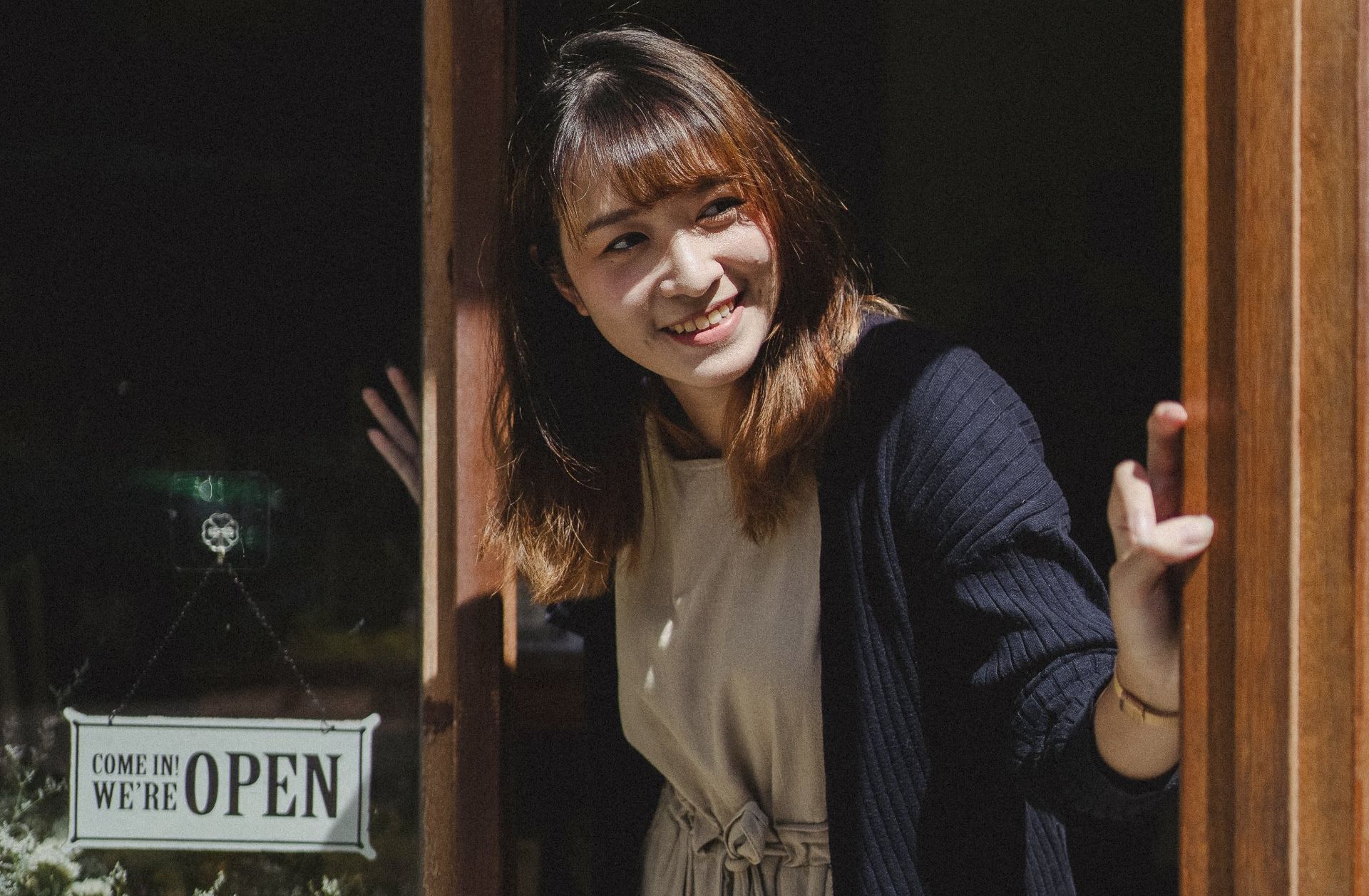 Smiling woman leaning out door next to open sign