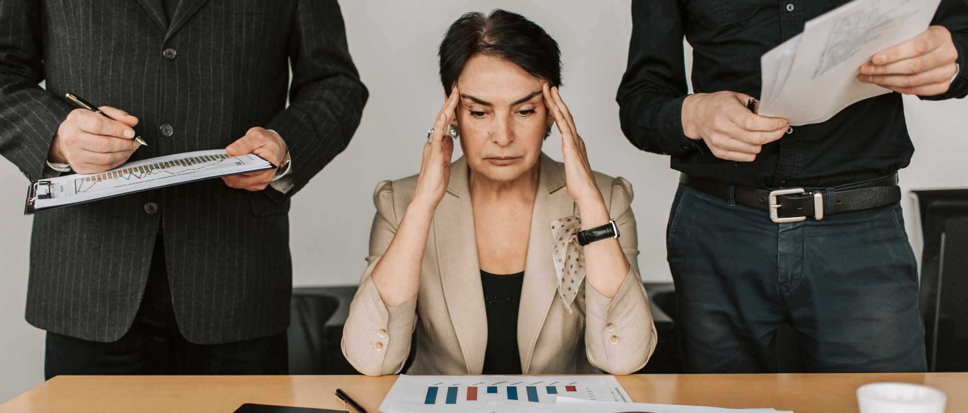 Woman rubbing fingers against her temples  surrounded by two men showing her paperwork