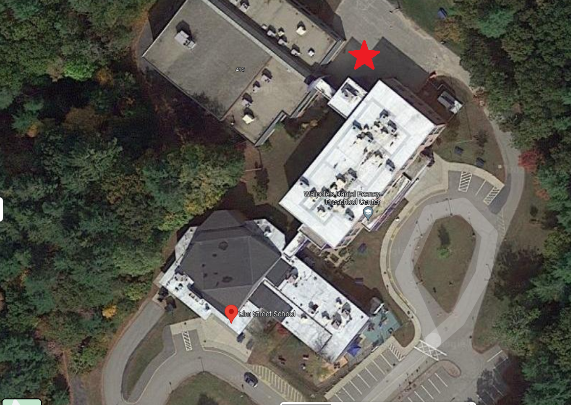 Aerial view of two buildings beside a curving driveway and trees, marked with a red star and pin.