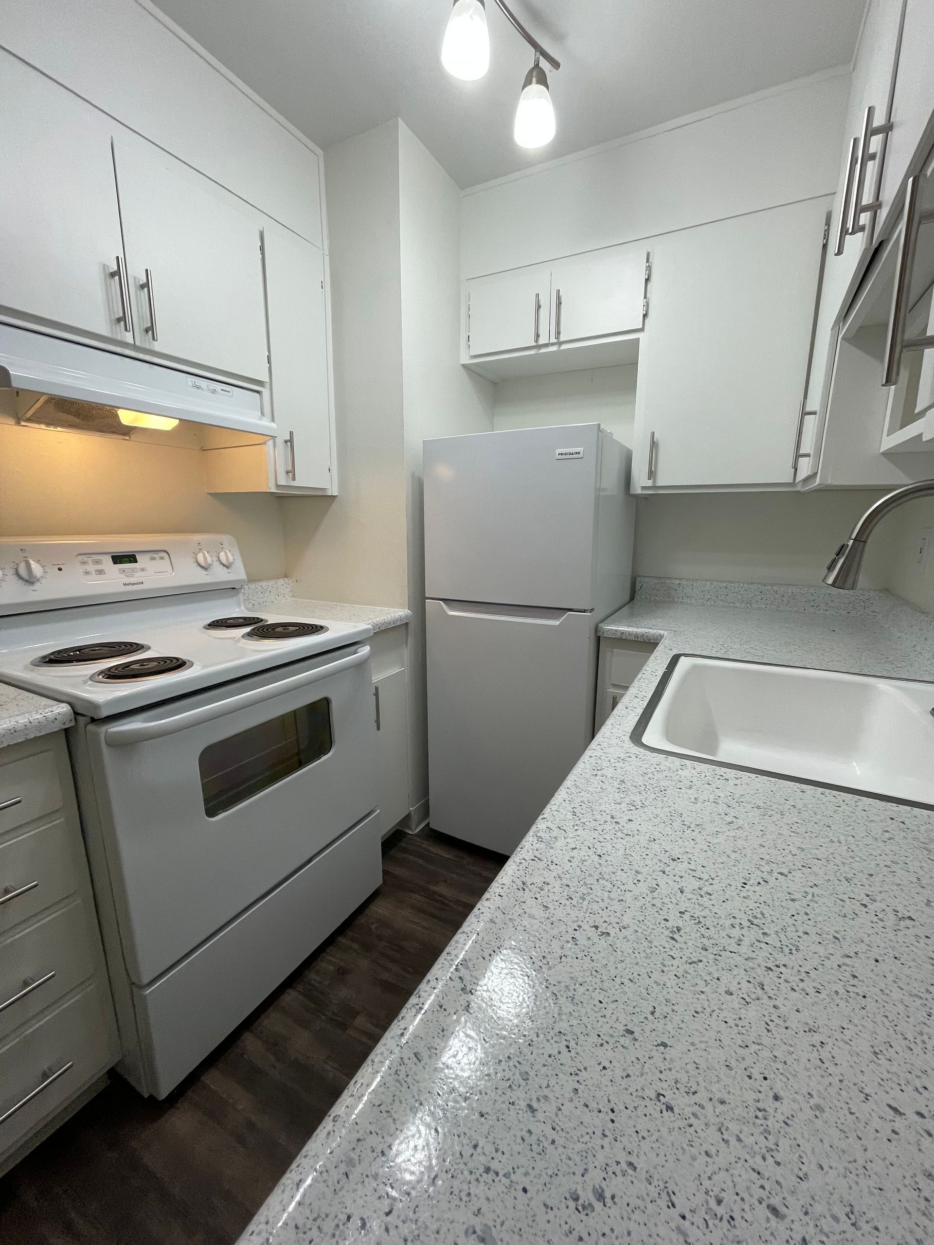 Compact white kitchen with stove, refrigerator, and sink in a narrow galley layout