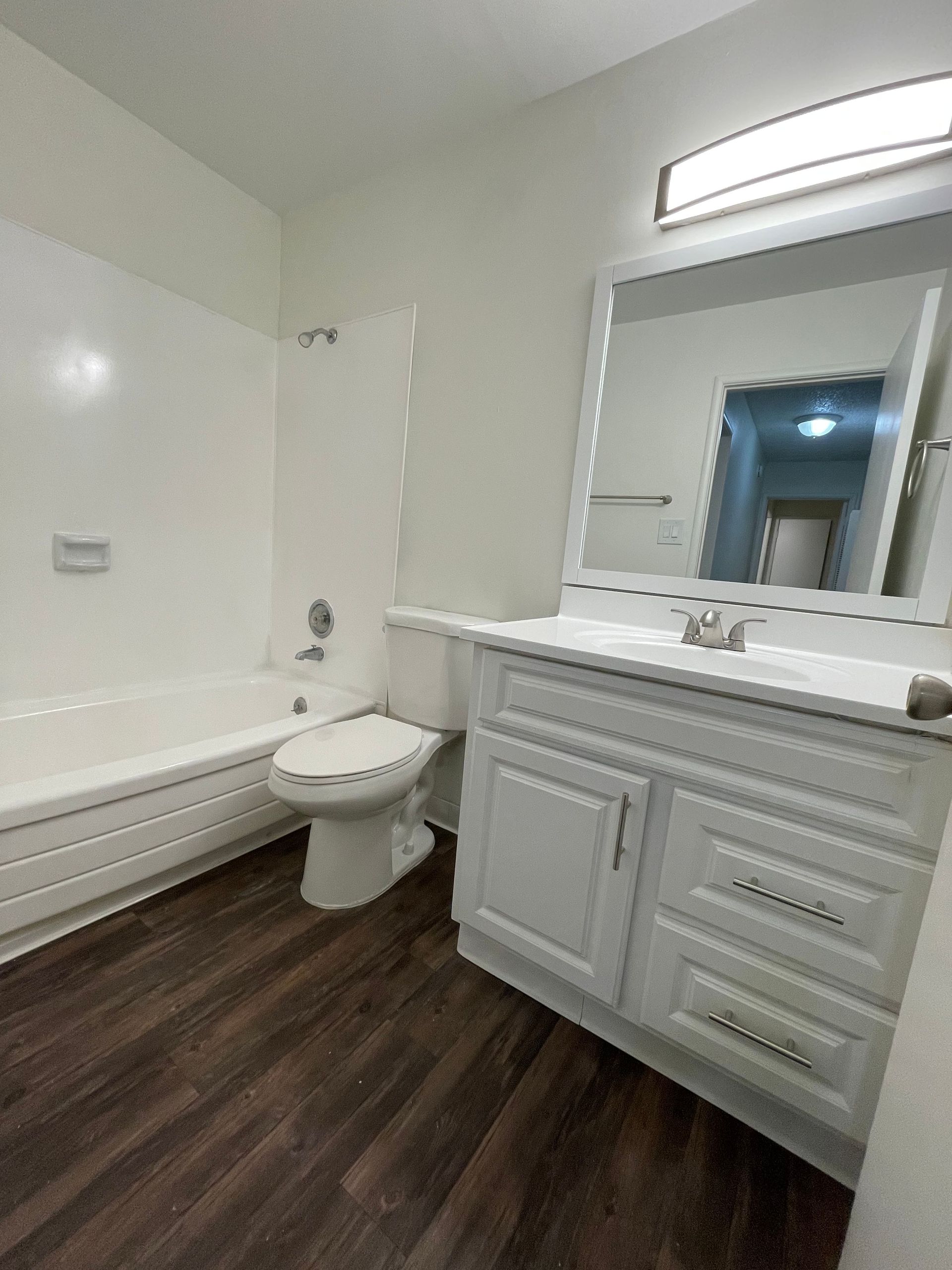 Small bathroom with white vanity, toilet, bathtub, and dark wood-look flooring