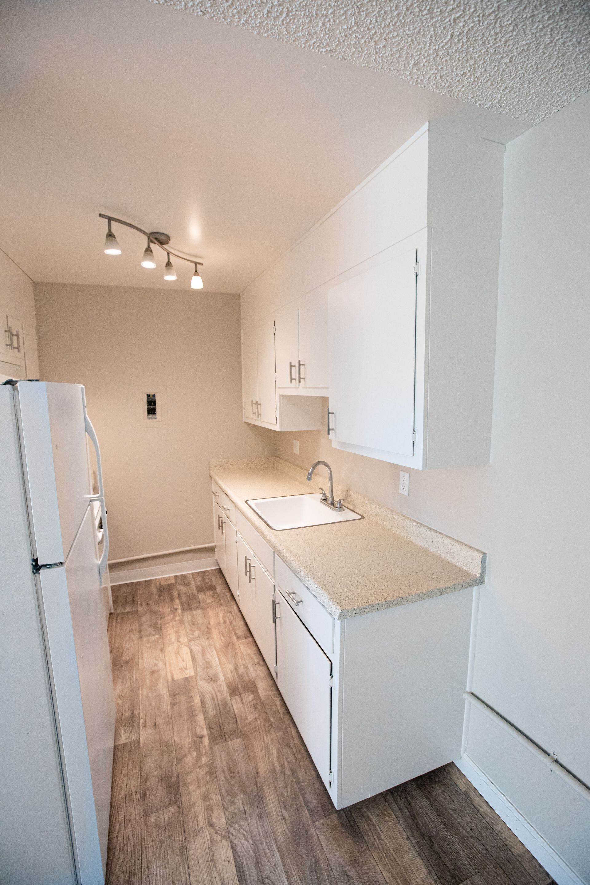 Bright narrow galley kitchen with white cabinets, beige counters, and wood-look flooring.