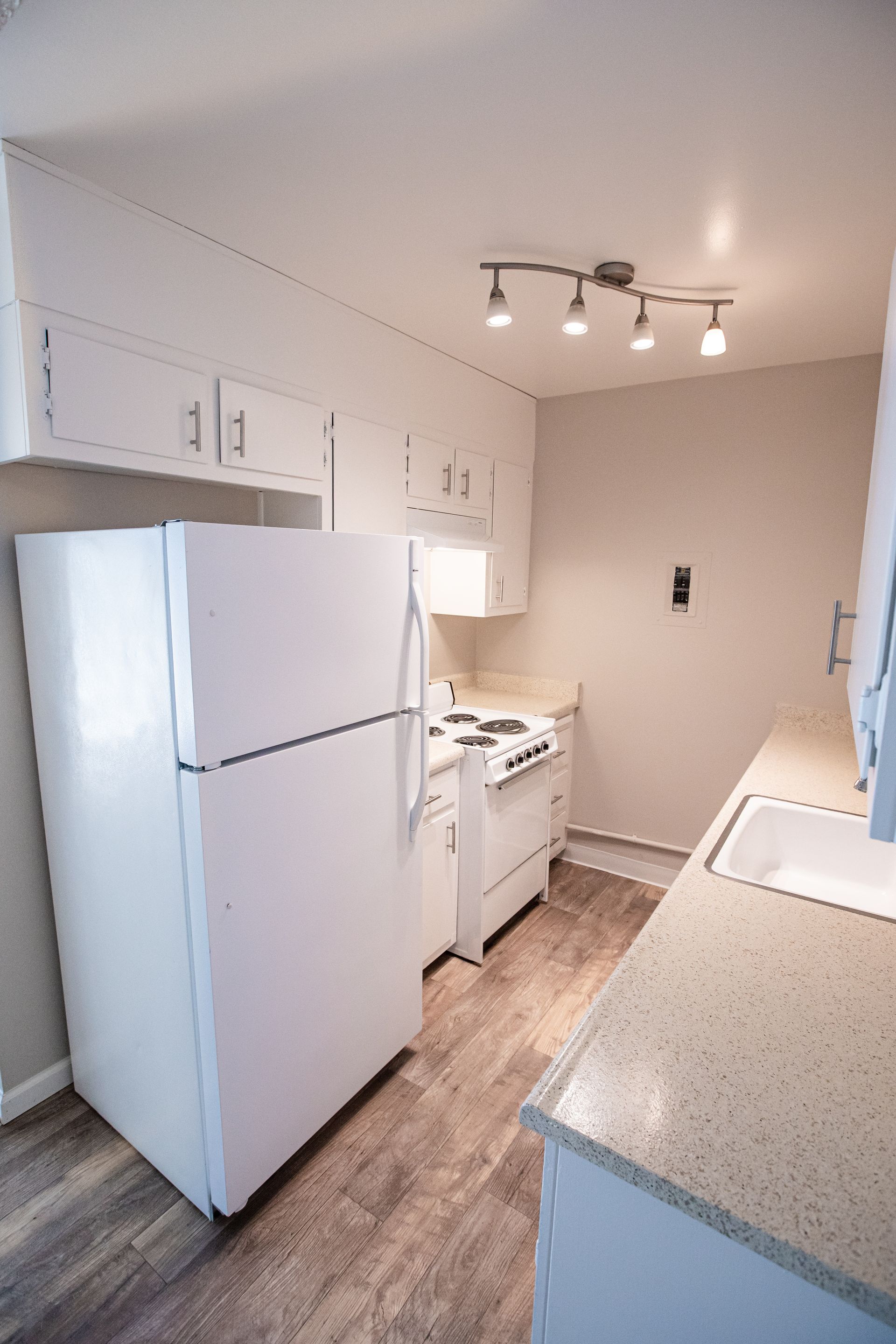Narrow white kitchen with refrigerator, stove, cabinets, and speckled countertops under track lighting