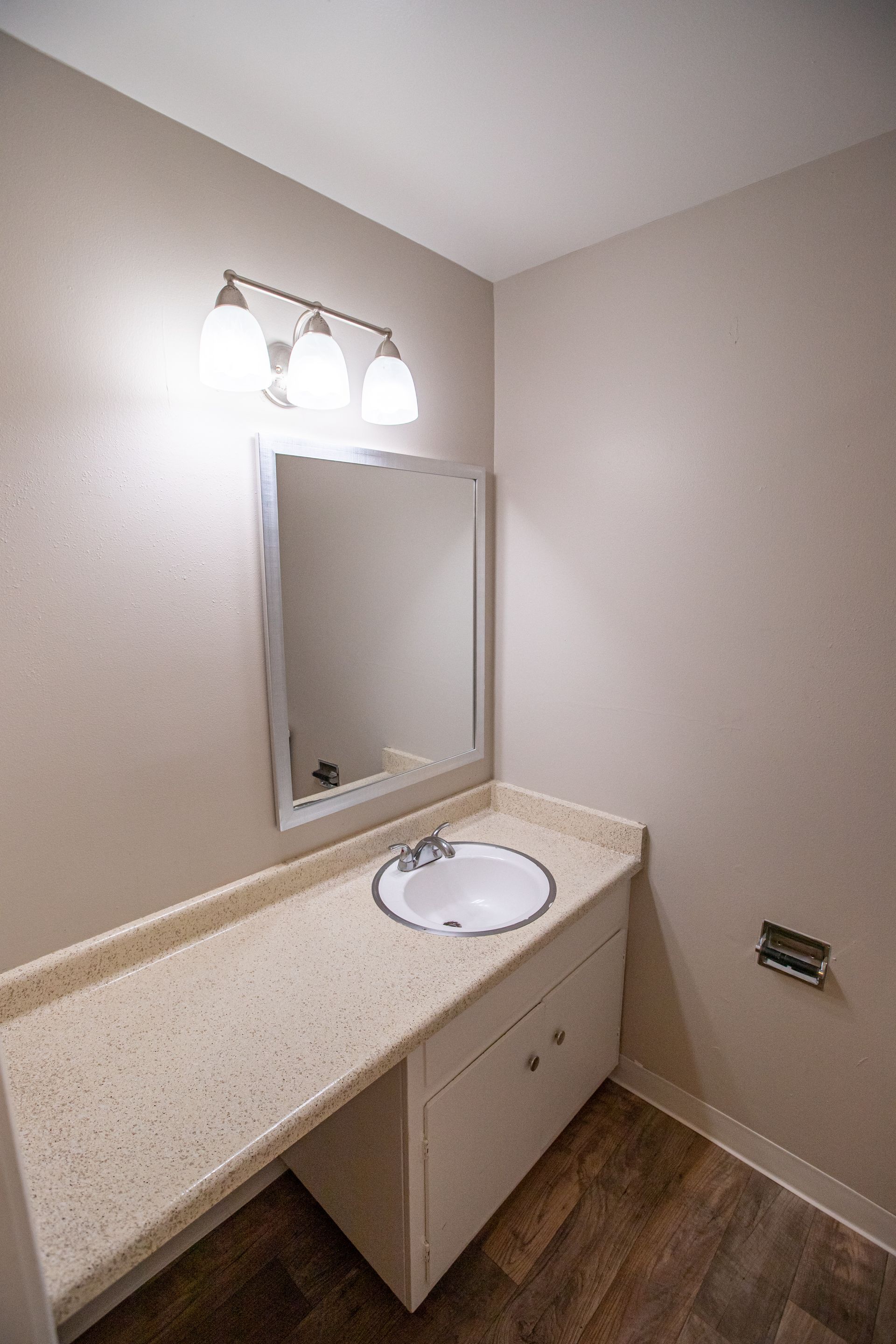 Small beige bathroom vanity with mirror, light fixtures, and white sink.