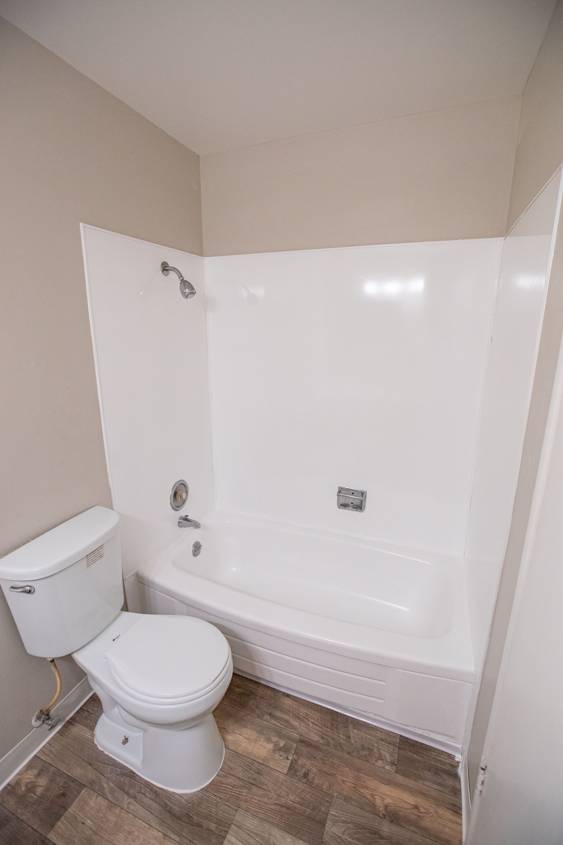 Small bathroom with a white toilet beside a white bathtub and beige walls.