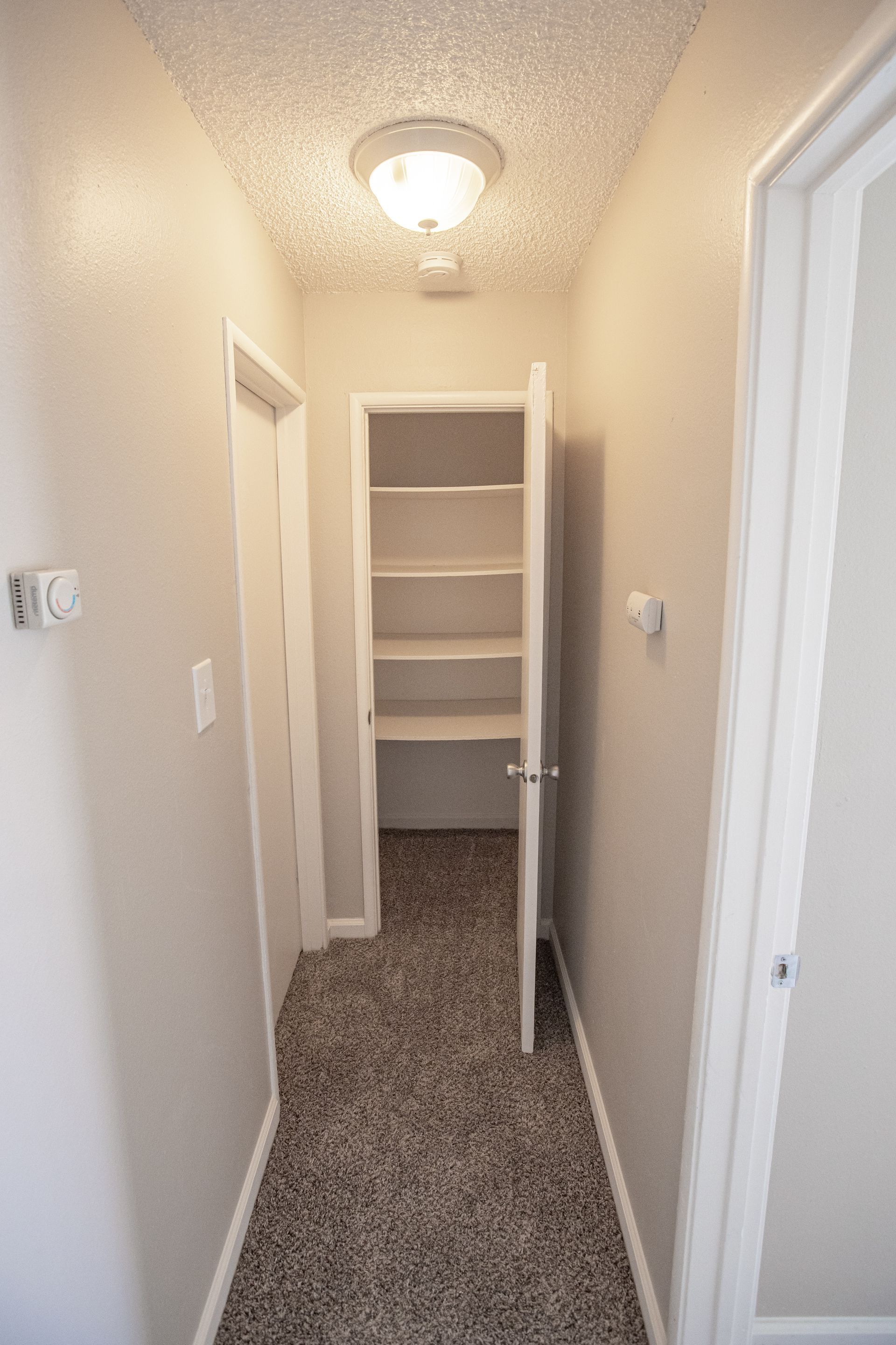 Narrow beige hallway with carpet and a built-in shelving nook at the end.