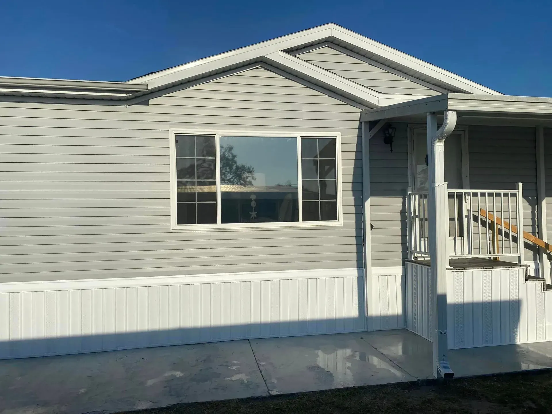 Light gray mobile home with white trim and a concrete patio. Light gray mobile home with white trim and a concrete patio.