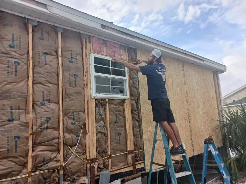 Man on ladder, installing siding on house with exposed insulation and window. Sunny day. Man on ladder, installing siding on house with exposed insulation and window. Sunny day.