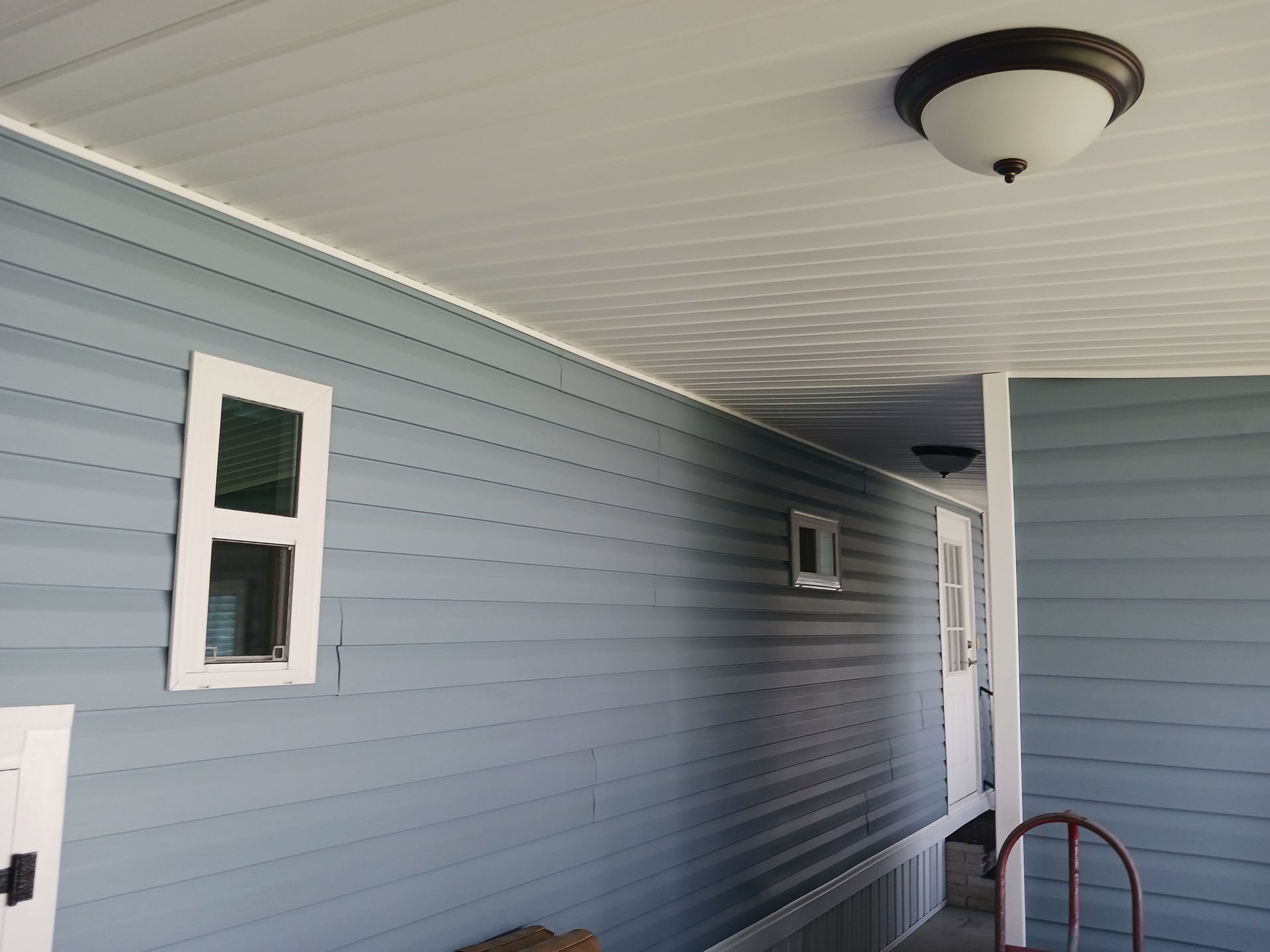 Blue siding on a building with white trim around windows. Ceiling has a light fixture. Blue siding on a building with white trim around windows. Ceiling has a light fixture.