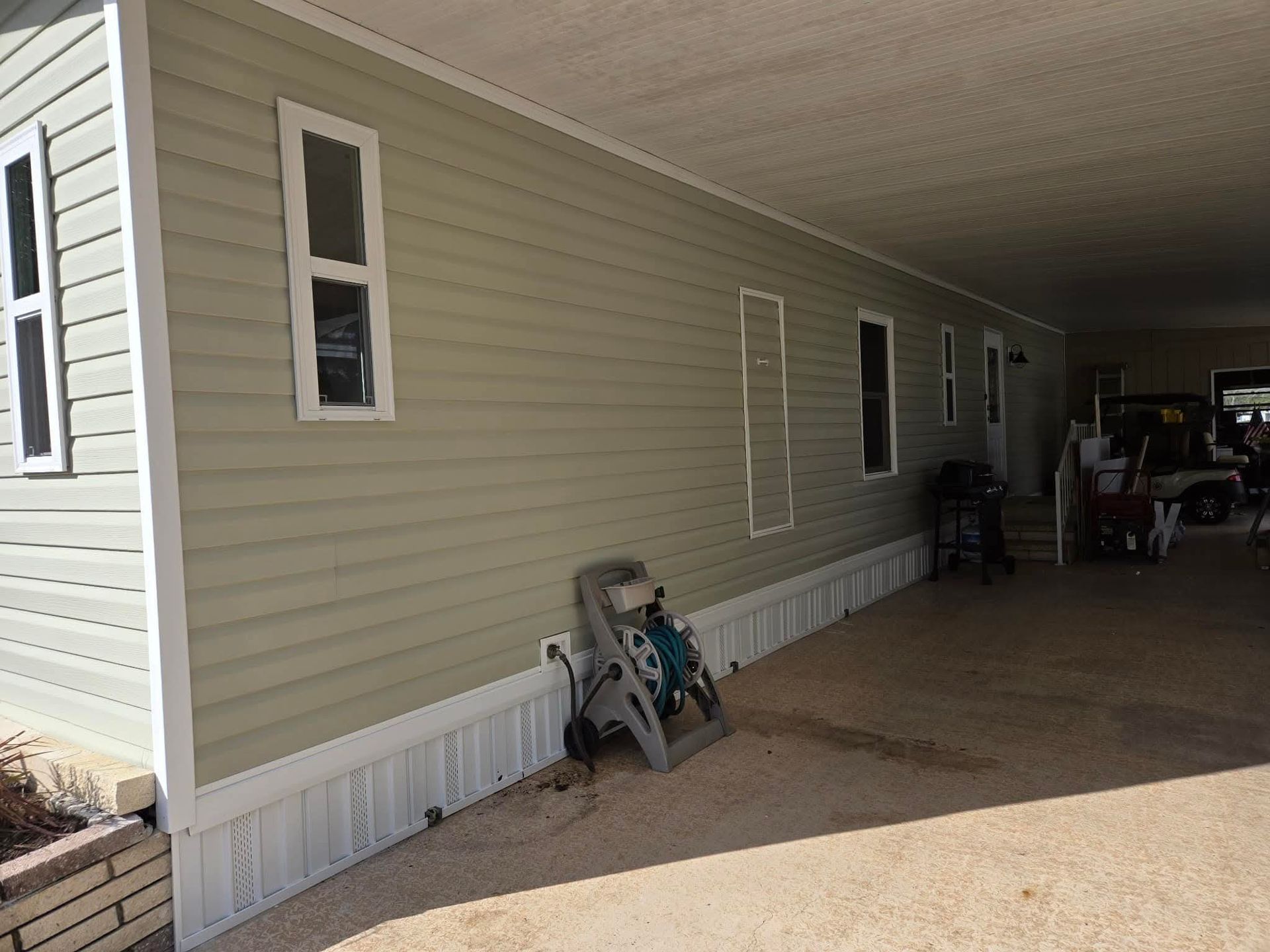 Beige mobile home exterior with white trim, carport. A gray step stool leans against the wall. Beige mobile home exterior with white trim, carport. A gray step stool leans against the wall.