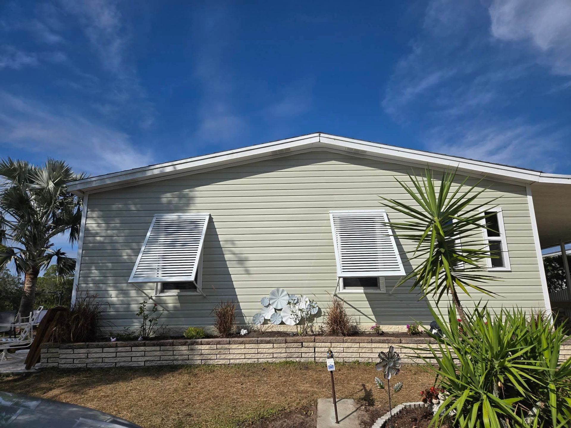 Light green house with shuttered windows against a bright blue sky, with surrounding landscaping. Light green house with shuttered windows against a bright blue sky, with surrounding landscaping.