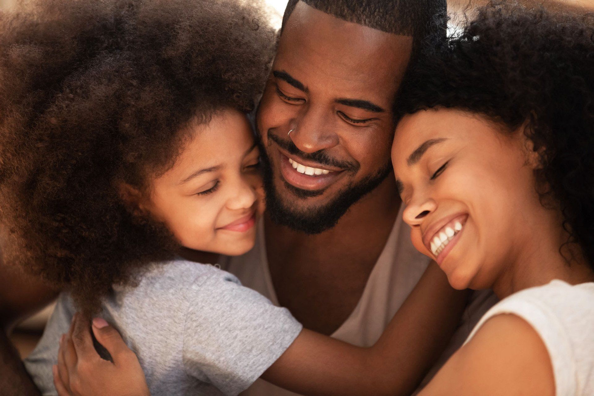 A man , woman and child are hugging each other and smiling.