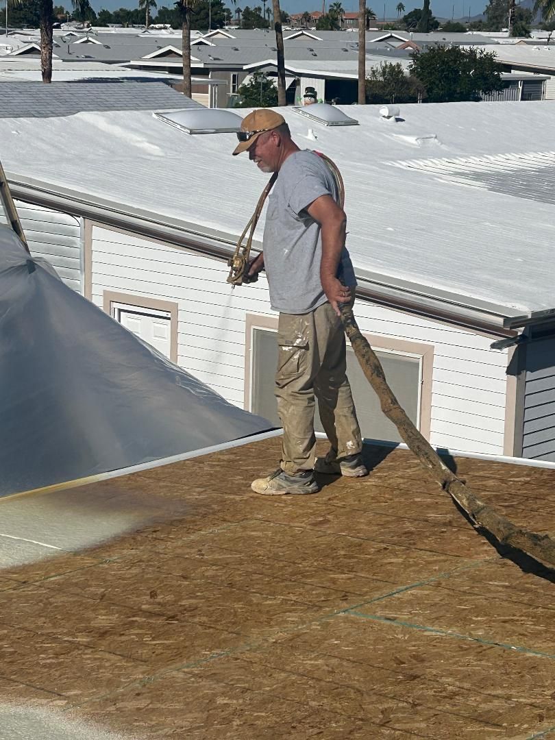 Worker standing on a rooftop beside rolled roofing material and white rooftops in the background