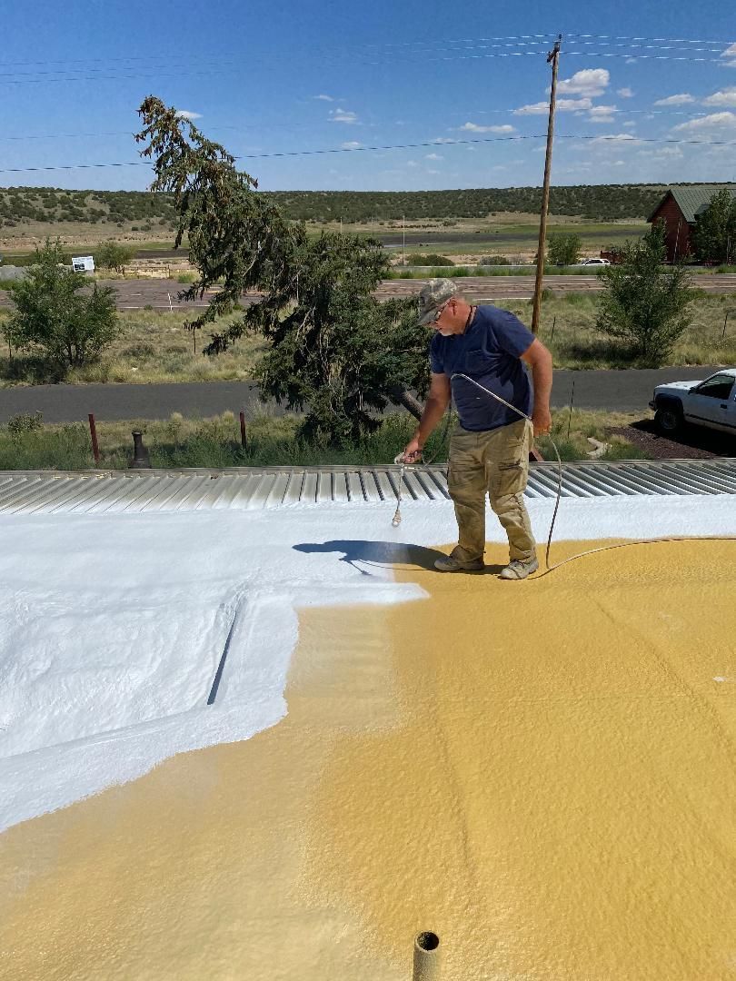 Worker rolling white and yellow coating on a flat rooftop under clear sky