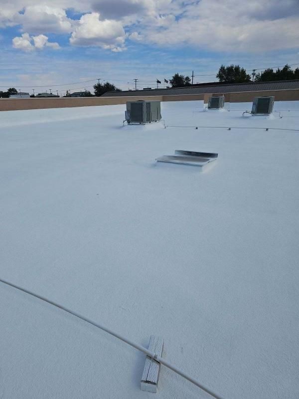 White flat rooftop with vents and a cable under a cloudy sky