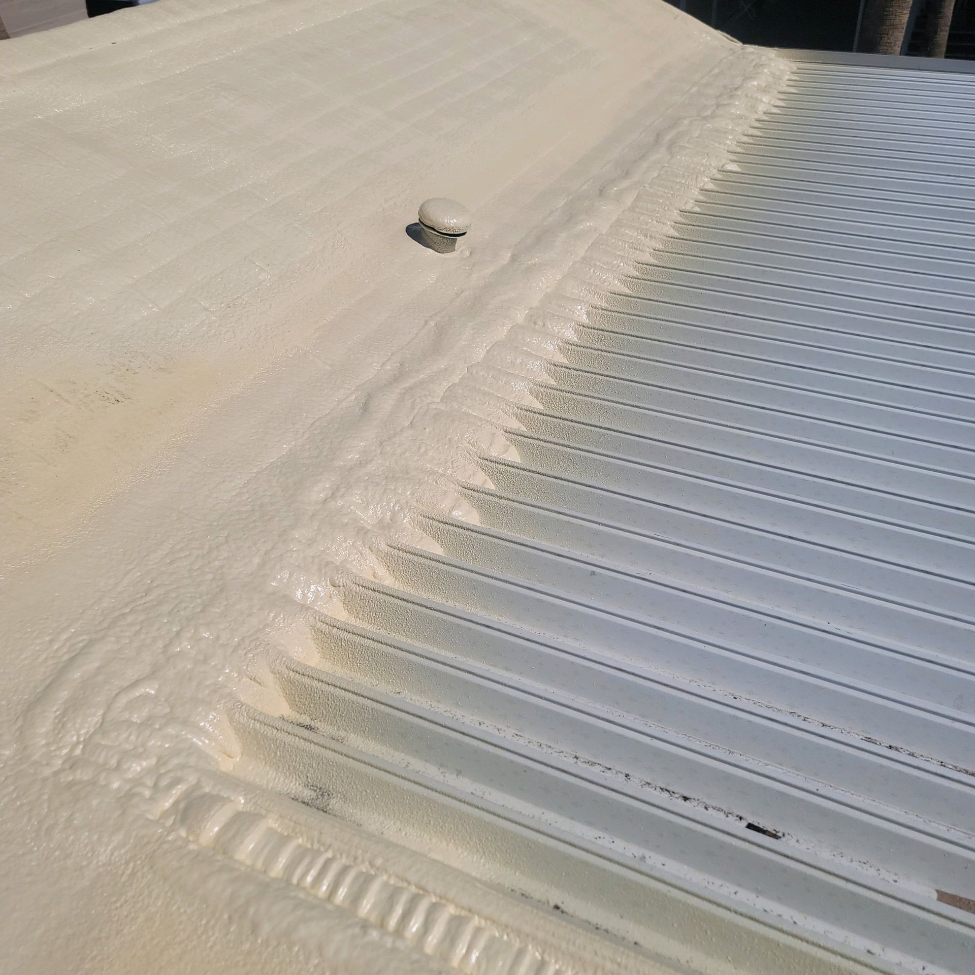A white rooftop with a small vent and a ridge of drifting snow beside metal panels.