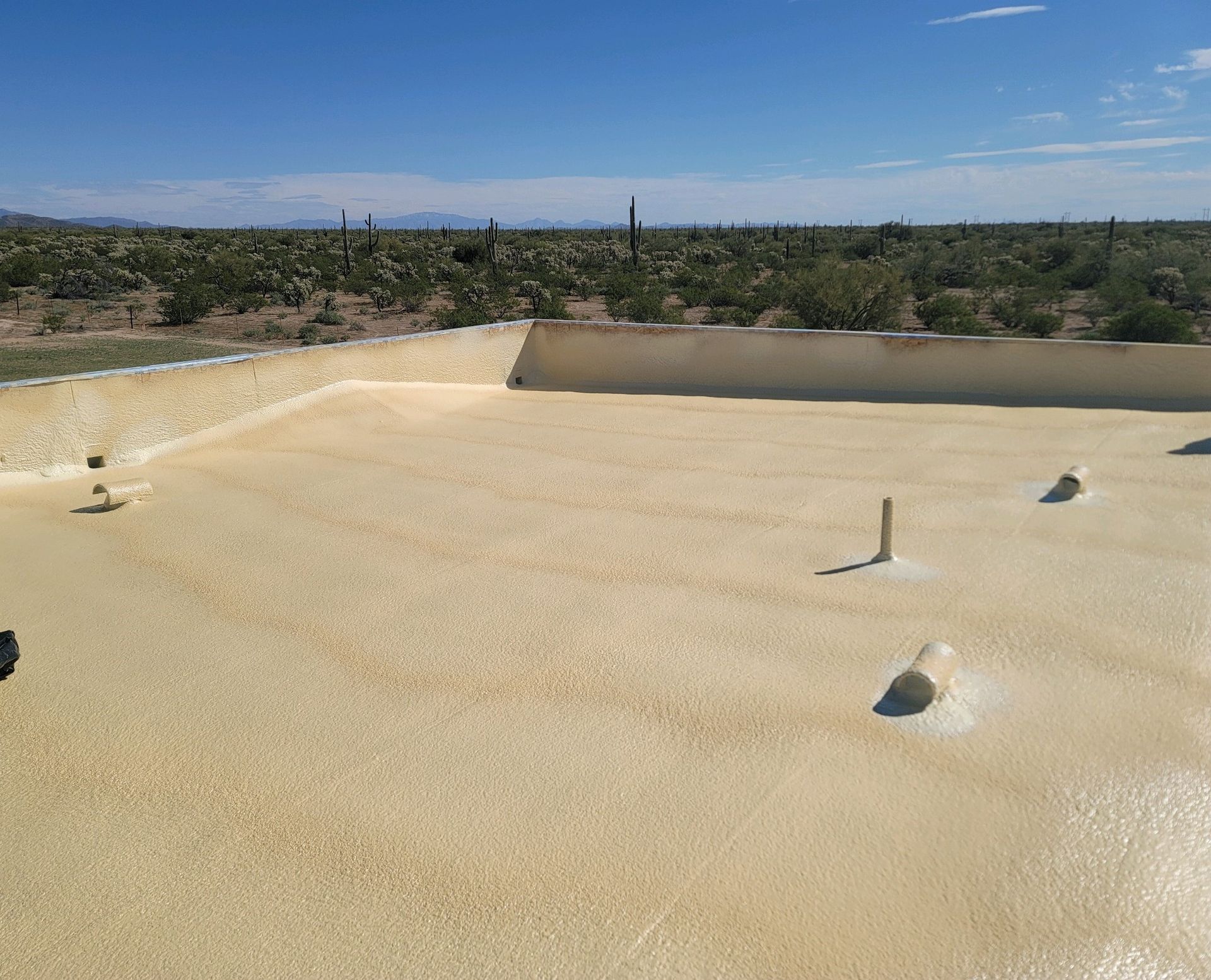 Empty beige rooftop with gravel surface, low parapet walls, and a desert landscape in the distance
